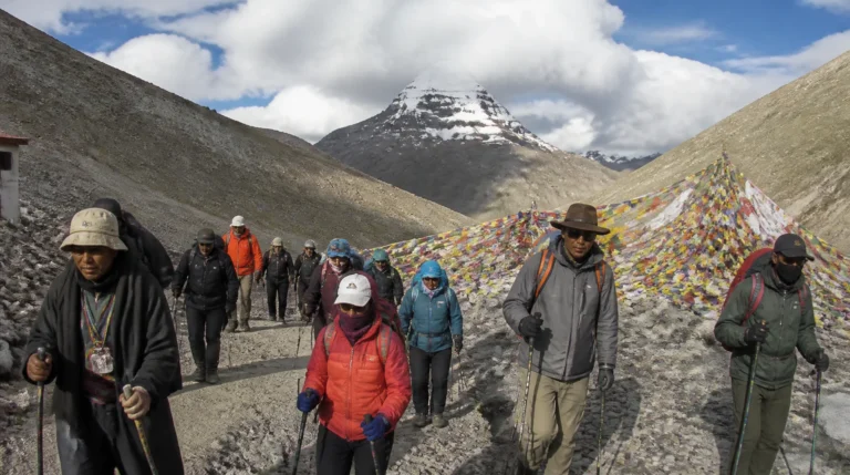 Pilgrims trekking the sacred Kora circuit of Mount Kailash at high altitude with prayer flags and Tibetan mountains in the background